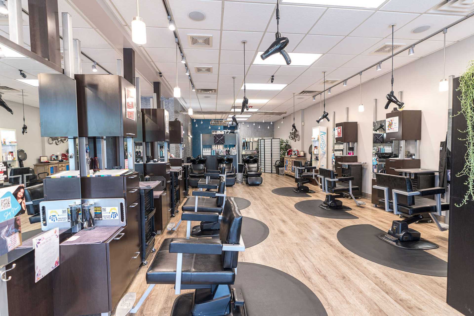 Modern hair salon with multiple styling stations, mirrors, and black chairs on a wooden floor.