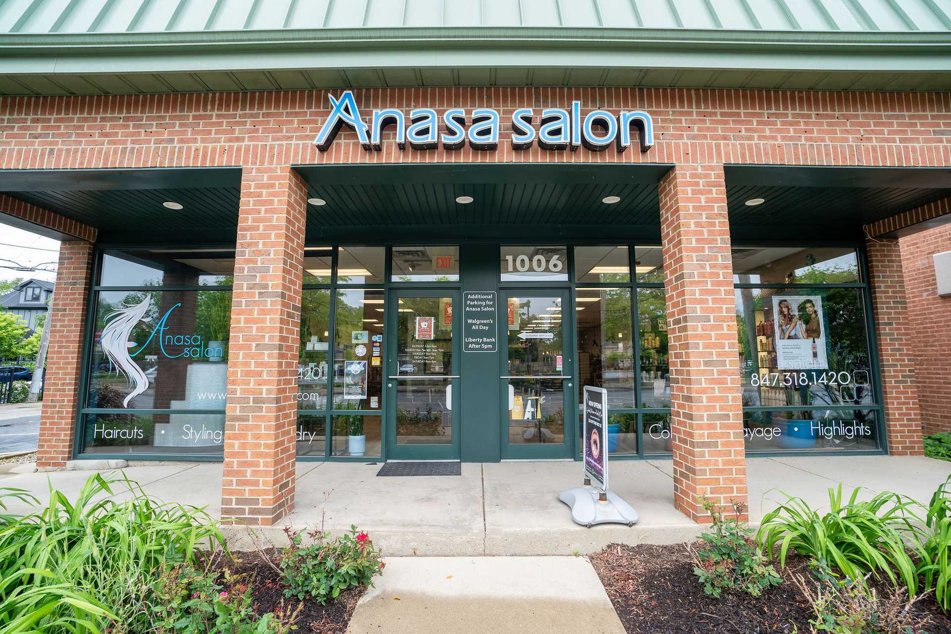 Entrance to Anasa Salon with glass doors and windows, displaying salon services and contact details.