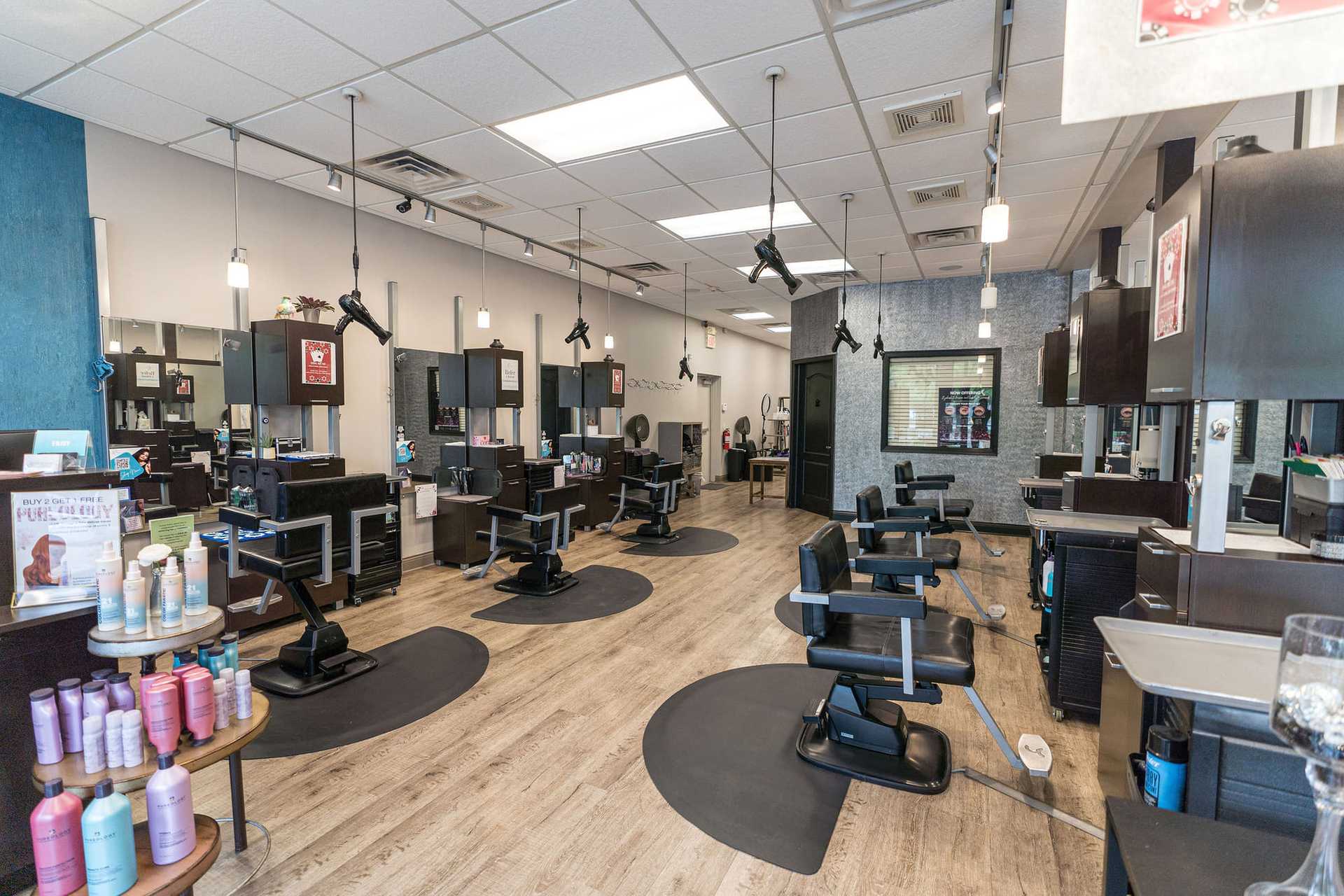 Modern, stylish hair salon with empty black chairs, mirrors, and various hair products on shelves.