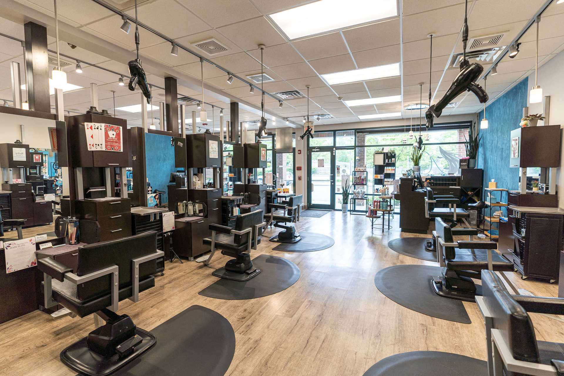 Modern hair salon with multiple styling stations, mirrors, and black chairs, empty and well-lit.